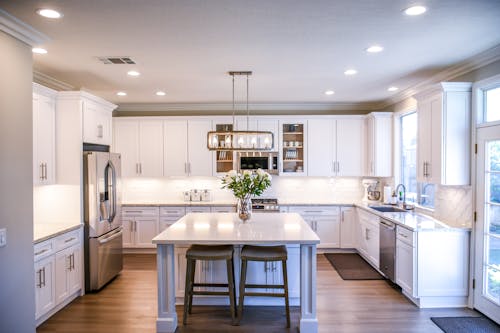 Free Spacious and elegant kitchen featuring white cabinetry, island, and stainless steel appliances. Stock Photo