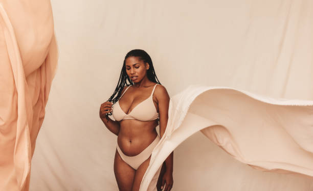 Curvy young woman posing in beige underwear Curvy young woman posing in beige underwear. Self-confident young woman standing against a studio background. Body positive young woman embracing her natural body and beauty. bra size 2 women stock pictures, royalty-free photos & images
