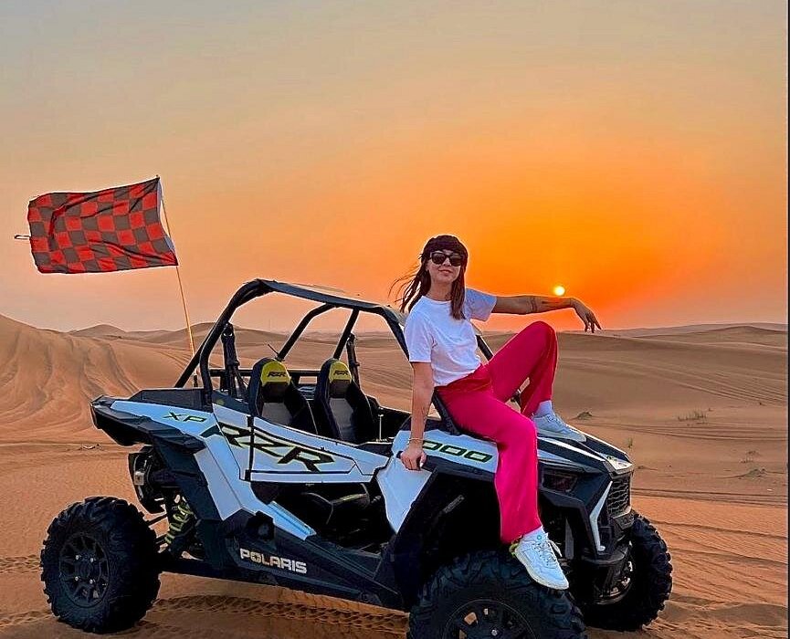 Woman posing beside a dune buggy during a thrilling Dubai desert adventure at sunset.